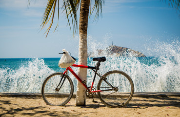 Fototapeta premium Waves splashing red bicycle leaning on palm tree in the beach