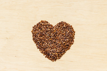 buckwheat groats heart shaped on wooden surface.