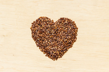 buckwheat groats heart shaped on wooden surface.