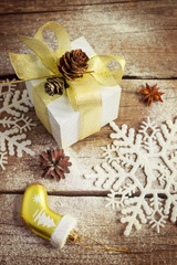 Fototapeta na wymiar Present in festive packaging with gold bow, snowflakes, fir cone