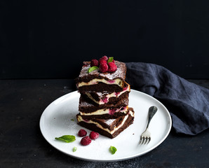 Brownie-cheesecake tower with raspberries on white plate, black