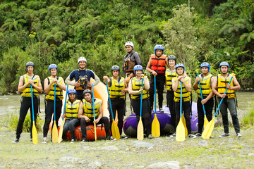 A large group of young people, ready for adventure, building teamwork as they go rafting on the...