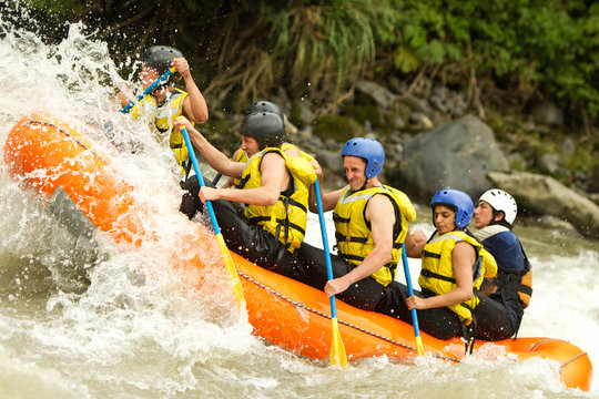 A team of adventurers in helmets navigating white rapids on a raft in Ecuador, surrounded by rocks and the rush of extreme whitewater action.
