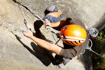 A close-up image of an athletic climber wearing a helmet, conquering extreme challenges while climbing up a mountain rock during an expedition.