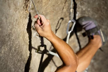 Fototapeten A man with strong muscles and sweating palms climbs a steep rock face, secured by a rope above. The adrenaline of the sport is palpable. © Ammit