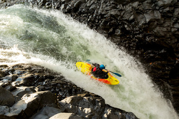 A thrilling image of a kayaker navigating through the extreme whitewater of a waterfall, showcasing the dynamic sport of rafting in nature.