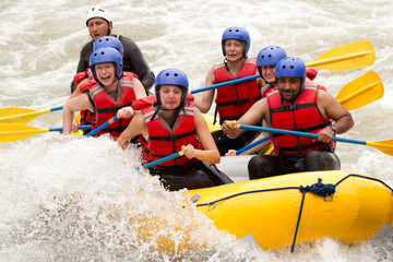 Fototapeta na wymiar A group of adventurous people in helmets and life jackets navigating a white water rafting adventure with their experienced guide team on a rushing river.