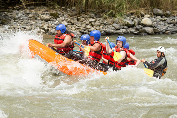 A group of friends wearing red life jackets navigating through white water rapids on a rafting...