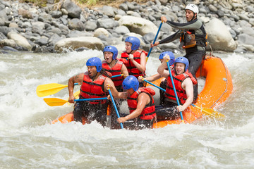 A team of people in a white water raft navigating through thrilling rapids on a fast-flowing river,...