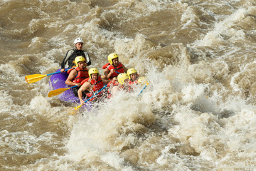 An assorted assembly of male and female tourists experiences the thrill of whitewater river rafting in Ecuador led by a seasoned pilot navigating the challenging currents