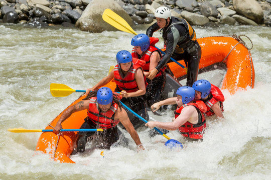 A group in life jackets and helmets paddle an orange raft through turbulent whitewater rapids with a guide in Ecuador, splashing water and rocky banks framing the adventure.