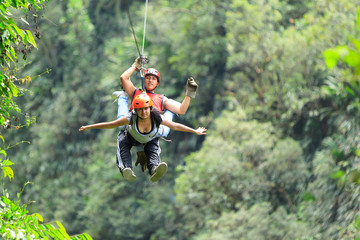 A couple on an adventure in the jungle of America, gliding through the canopy on a zip line, hanging from a wire as they travel. © Ammit