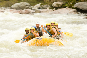 A diverse group of men and women in Ecuador enjoying the thrill of white water rafting together, guided by an experienced instructor through challenging rapids.