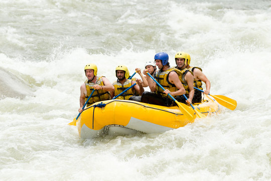 A group of five in life vests and helmets navigate a yellow raft through churning white-water rapids in Ecuador, focused expressions capturing the thrill and energy of whitewater rafting.