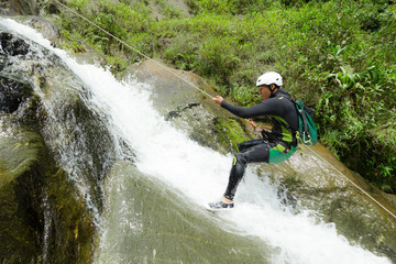 A group of adventurous individuals rappelling down a steep canyon wall with the help of a guide,...