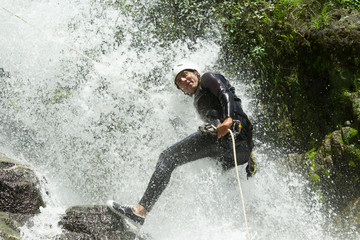 A male adventurer in neoprene gear rappelling down a waterfall in Chama Canyon, an extreme sport guided by a professional canyoning expert.