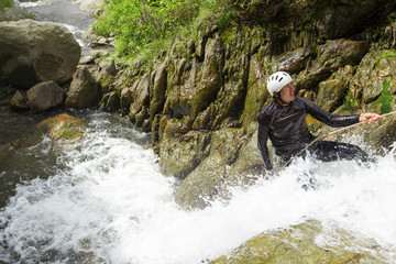 A daring athlete rappelling down a steep canyon wall, descending towards the rushing water below, ready to conquer the aquatic challenge.