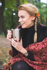 Young woman drinking hot tea or coffee outdoor in autumn park