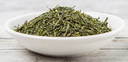 Fototapeta na wymiar Dried green tea leaves in white bowl over wooden background