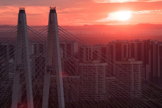 Pylons cable-stayed bridge against the backdrop of urban residential district at sunrise.