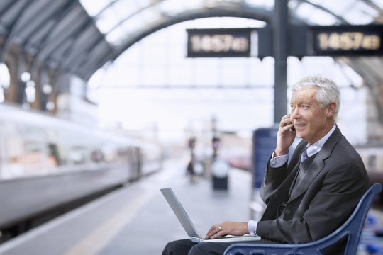 Senior businessman takes a mobile call on a train station platform.