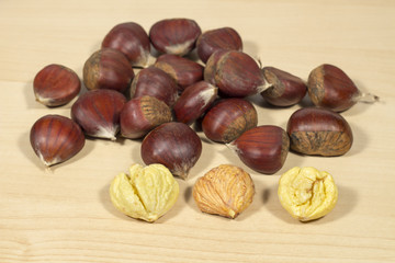 Several peeled chestnuts in front of other ones in shell, on a clear wood table