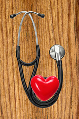Medical stethoscope and red heart on wooden table