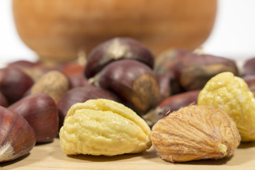 Several raw chestnuts, peeled or not, in front of a wooden bowl