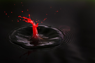 Beautiful image of a drop of red cream falling into dark water in the shape of a little man getting shot