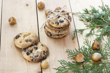 Homemade Christmas cookies with chocolate, nuts, cones, cinnamon and green arborvitae branch on a wooden table