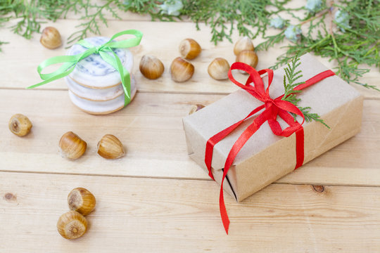 Christmas gift and cookies, nuts, cones, cinnamon and green arborvitae branch on a wooden table