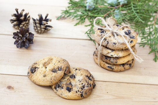 Homemade Christmas cookies with chocolate, nuts, cones, cinnamon and green arborvitae branch on a wooden table