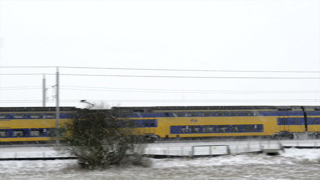 Dutch NS passenger train driving through a snowy winter landscape on a cold winter day.
