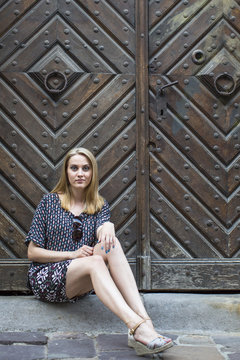 Pretty young woman sitting on the pavement outside an ancient wooden door.