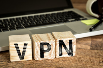 VPN (Virtual Private Network) written on a wooden cube in front of a laptop