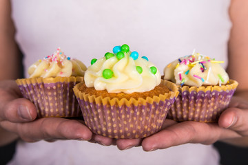 three sweet colorful cupcakes with butter cream in female hands