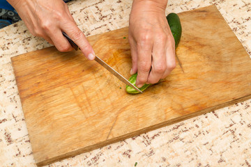 The chef cuts the cucumber on a wooden  Board.