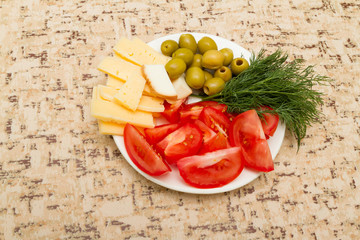 Cheese tomato green olives dill on a white plate on the  table.