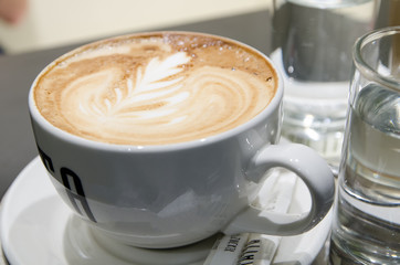 a large cup of coffee with foam on a saucer and a glass of water