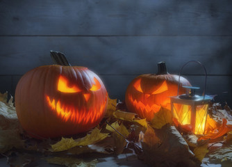 Spooky pumpkins jack o lantern among dried leaves on wooden fence