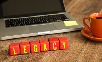 Legacy written on a wooden cube in front of a laptop
