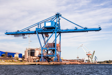 Fototapeta na wymiar Massive blue cranes unload cargo in a seaportduring sunset