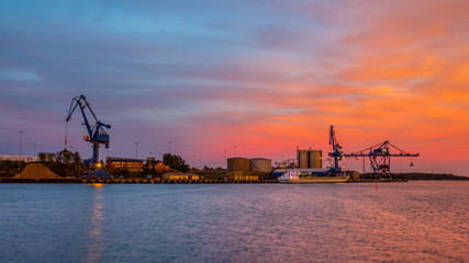 Fototapeta na wymiar Massive blue cranes unload cargo in a seaport during sunset