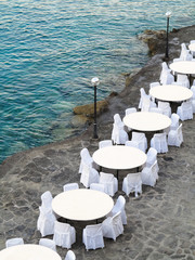 Open air restaurant near sea, white chairs and tables