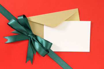 Red satin bow gift ribbon with greeting card in envelope for birthday or christmas present on red...