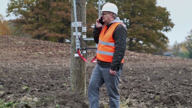 Electrical engineer with cell phone at outdoor near high voltage stake