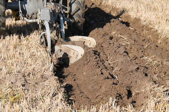 A Farming Plough Cutting a Deep Furrow in a Field.
