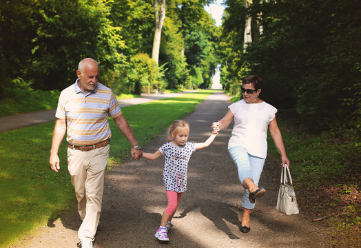 Grandparents With Grandchild walking together in the park