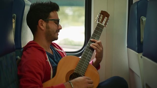 Great slow motion of young man playing guitar inside a train