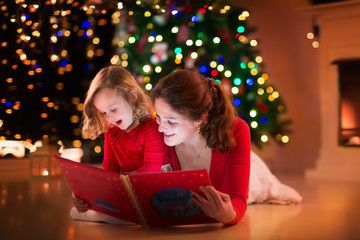 Fototapeta na wymiar Mother and daughter reading at fire place on Christmas eve